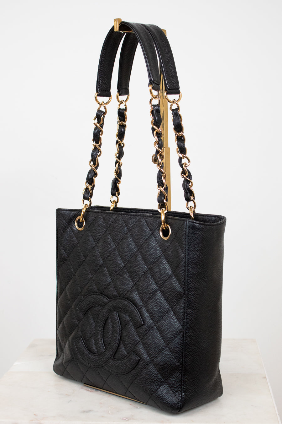 A black quilted leather tote bag with gold-tone hardware, featuring a large embossed interlocking CC logo on the front and dual top handles, shown on a light neutral background.