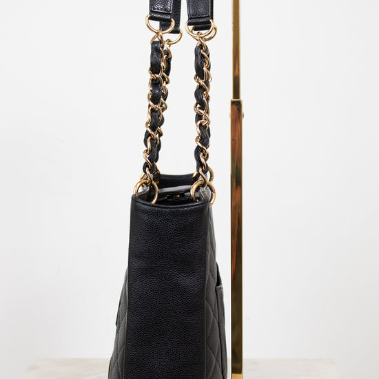 A black quilted leather handbag with gold-tone chain and strap details, displayed on a gold metal stand against a white background.