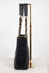 A black quilted leather handbag with gold-tone chain and strap details, displayed on a gold metal stand against a white background.