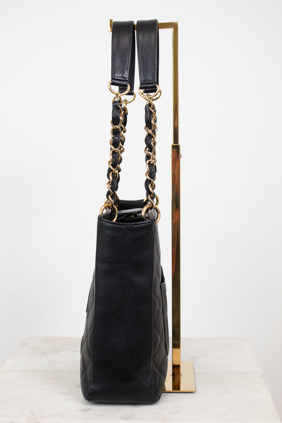 A black quilted leather handbag with gold-tone chain and strap details, displayed on a gold metal stand against a white background.