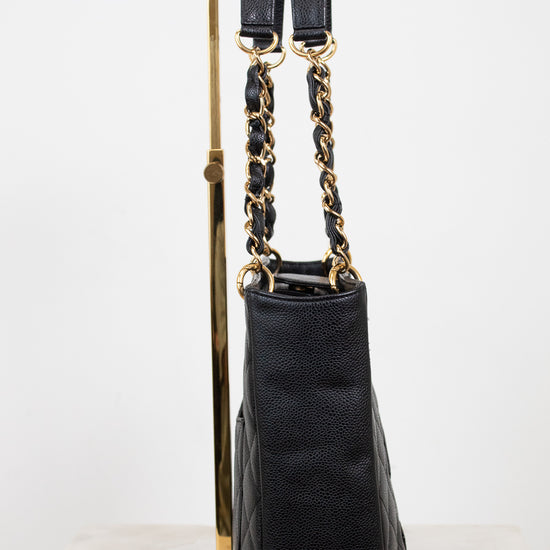 A black quilted leather handbag with gold-tone chain and strap hardware, displayed upright on a gold stand against a white studio background.