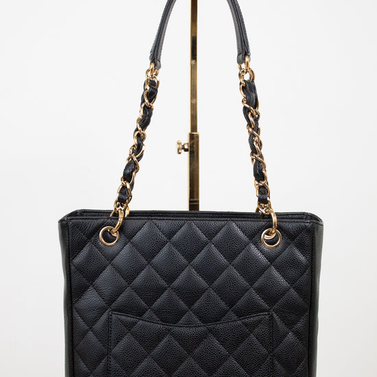 A black quilted leather tote bag with gold-tone chain handles and gold hardware, displayed on a stand against a white studio background.