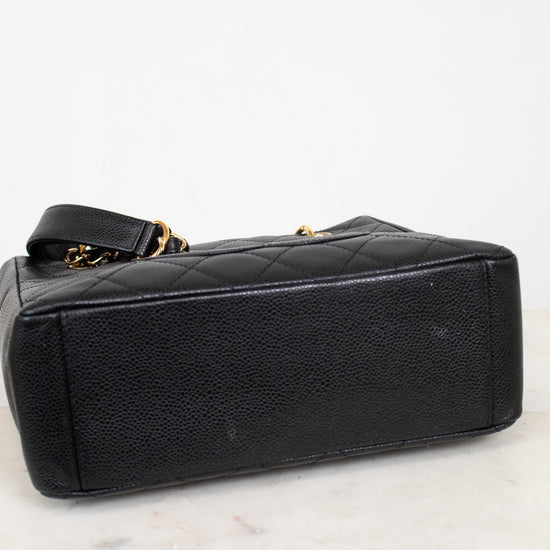 A black quilted leather handbag with gold-tone chain accents, shown from a side angle on a white marble surface against a white background.
