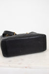 A black quilted leather handbag with gold-tone chain accents, shown from a side angle on a white marble surface against a white background.