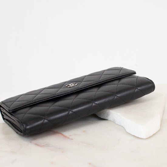 A black quilted leather wallet with a silver-tone interlocking CC logo, resting on a white marble block against a white background.