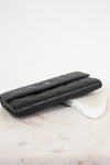 A black quilted leather wallet with a silver-tone interlocking CC logo, resting on a white marble block against a white background.