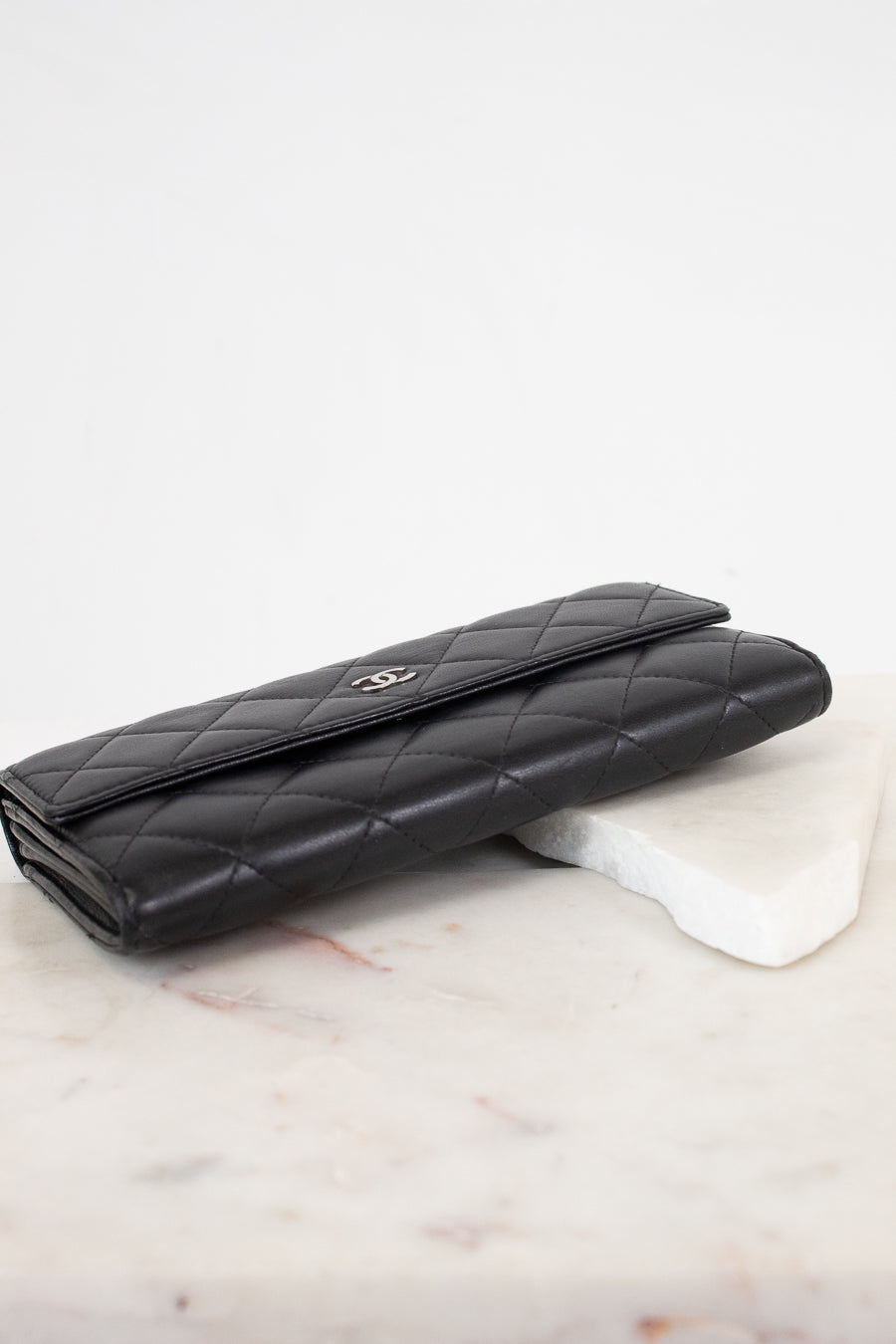 A black quilted leather wallet with a silver-tone interlocking CC logo, resting on a white marble block against a white background.