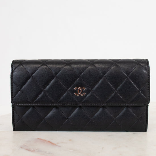 A black Chanel quilted leather wallet with a gold CC turn-lock, on a marble platform, against a white background.