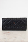 A black Chanel quilted leather wallet with a gold CC turn-lock, on a marble platform, against a white background.