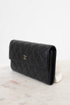 A black quilted leather wallet with a silver-tone interlocking CC logo, displayed on a white marble surface against a white background.