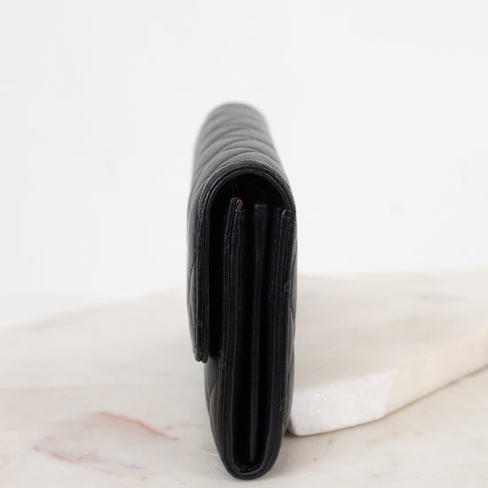 A black leather wallet standing vertically on a light marble surface against a white background.