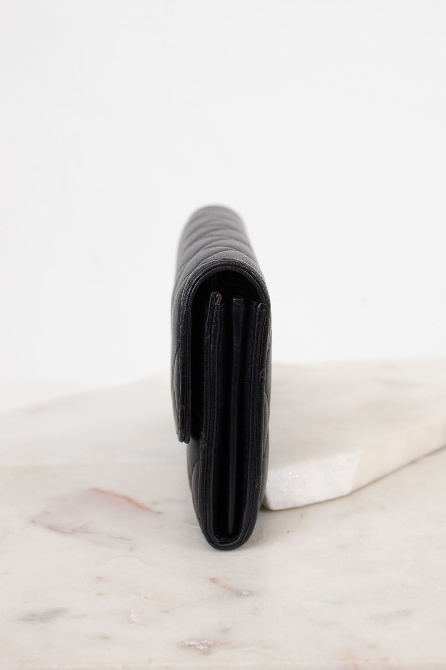 A black leather wallet standing vertically on a light marble surface against a white background.