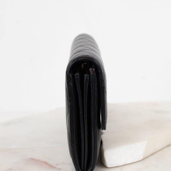 A black leather wallet standing vertically on a white marble slab against a clean white background.