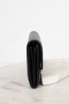 A black leather wallet standing vertically on a white marble slab against a clean white background.