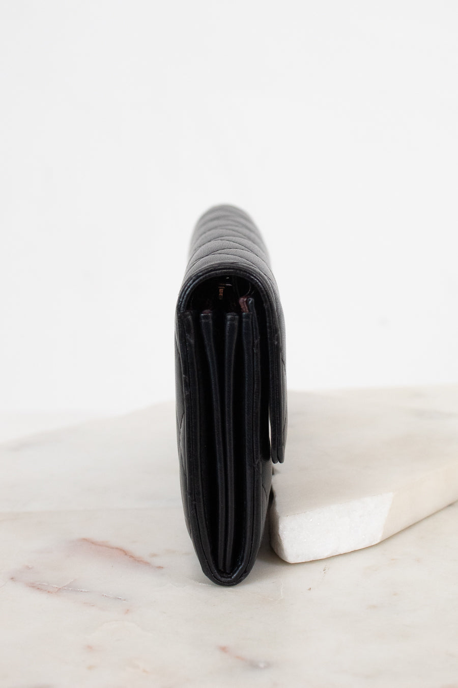 A black leather wallet standing vertically on a white marble slab against a clean white background.