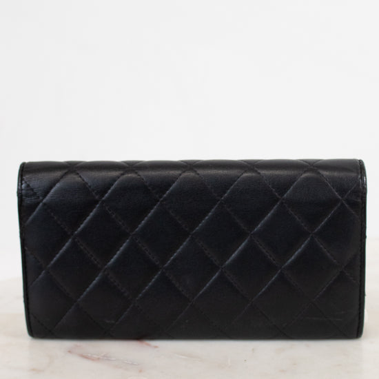 A black quilted leather wallet with a diamond pattern, resting on a white marble surface against a white background.