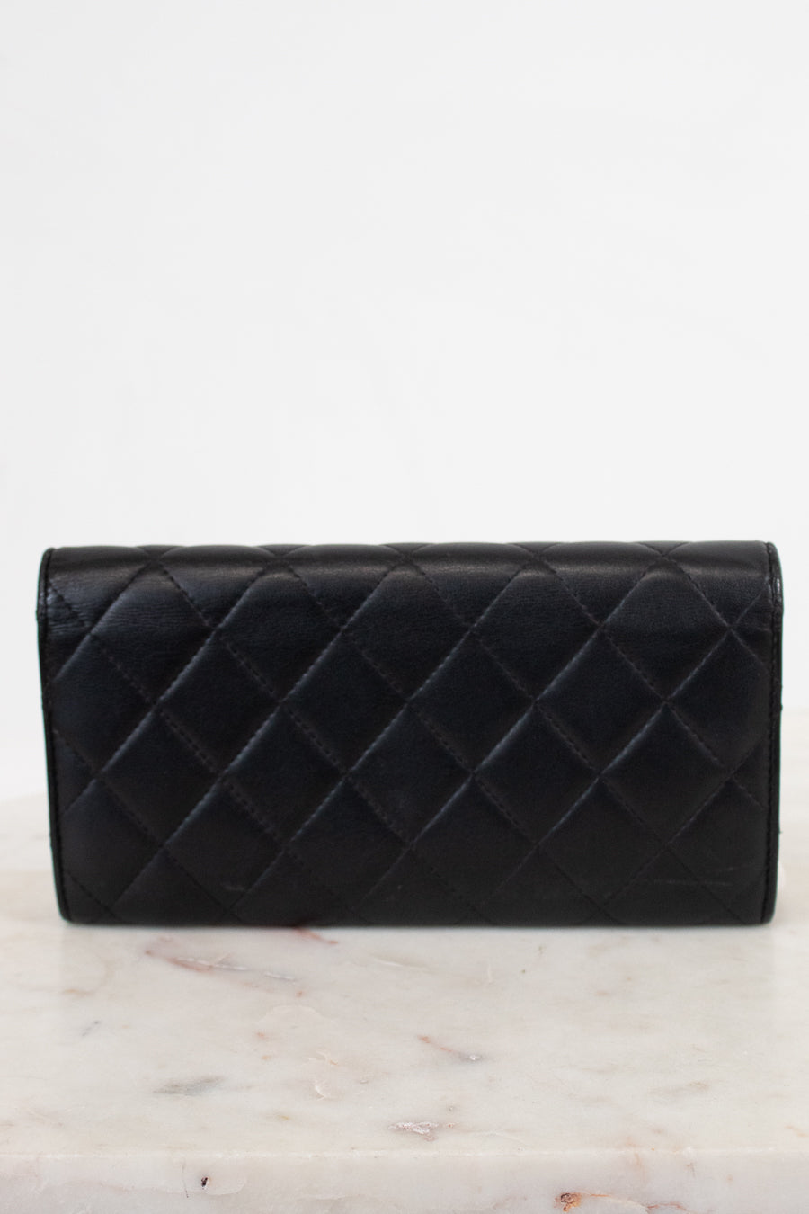 A black quilted leather wallet with a diamond pattern, resting on a white marble surface against a white background.
