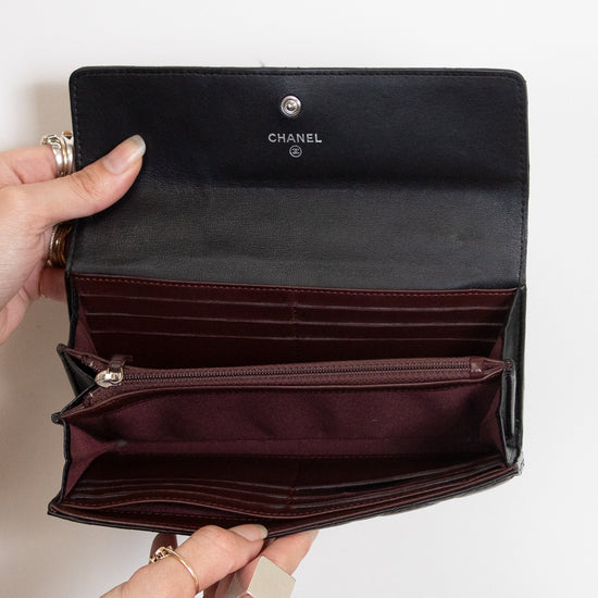 An open Chanel wallet in black leather with a burgundy interior, held by two hands against a plain white background.