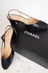 A pair of Chanel black leather slingback mule heels with a block heel and pointed toe, displayed next to their black Chanel shoebox on a light marble surface.