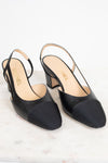 A pair of Chanel black leather slingback pumps with a low block heel and a contrasting black toe cap, displayed on a light marble surface against a white background.