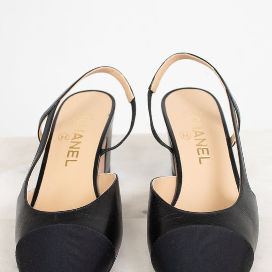 A pair of Chanel slingback high heels in black leather with a contrasting black suede toe cap, shown on a light marble surface against a white background.