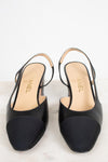 A pair of Chanel slingback high heels in black leather with a contrasting black suede toe cap, shown on a light marble surface against a white background.