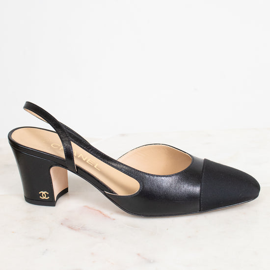 A single Chanel black leather slingback pump with a cap toe and block heel, resting on a white marble surface against a white background.