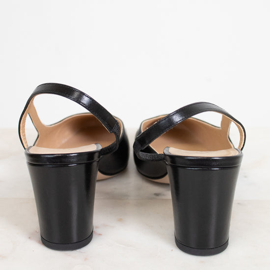 A pair of black leather slingback block-heel sandals shown from the back, resting on a light marble surface against a white background.