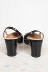 A pair of black leather slingback block-heel sandals shown from the back, resting on a light marble surface against a white background.