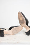 Black leather slingback high-heeled sandals shown from the sole, resting on a white marble surface against a white background.
