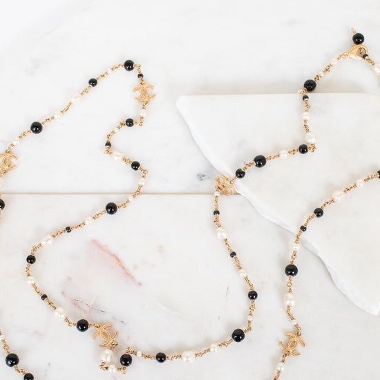 Long necklace with black and faux pearl beads on a marble surface