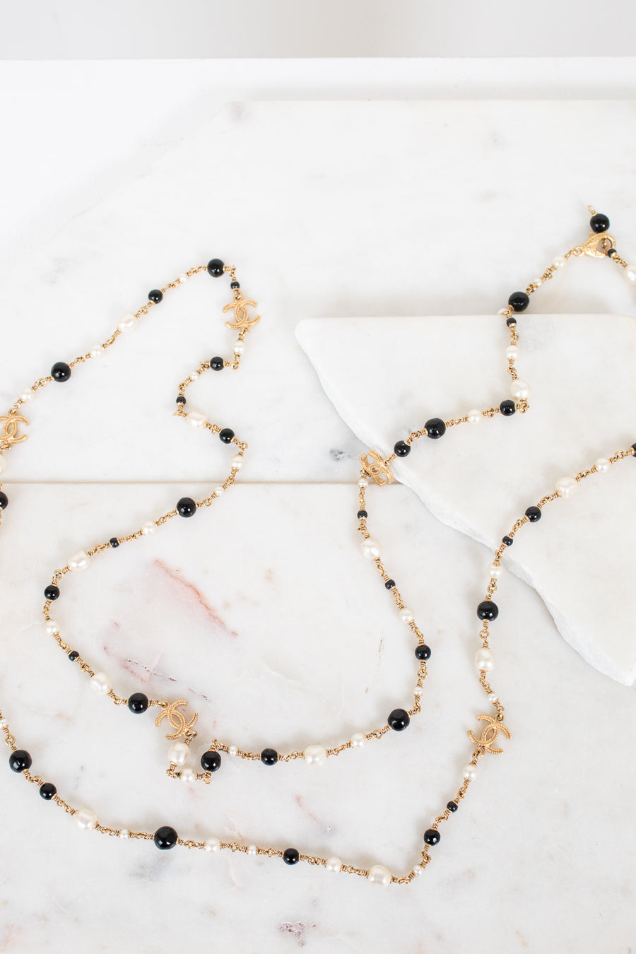 Long necklace with black and faux pearl beads on a marble surface
