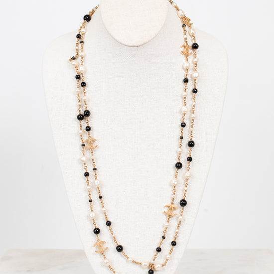 Multi-stacked necklace with black and faux pearl beads and gold-tone chain on a white stand