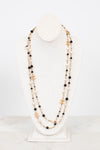 Multi-stacked necklace with black and faux pearl beads and gold-tone chain on a white stand