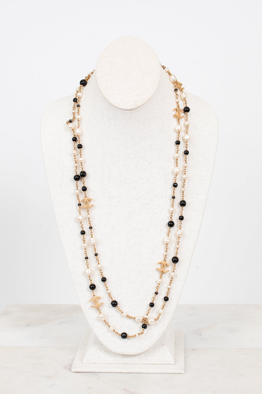 Multi-stacked necklace with black and faux pearl beads and gold-tone chain on a white stand