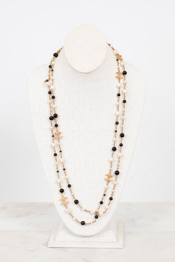 Multi-stacked necklace with black and faux pearl beads and gold-tone chain on a white stand