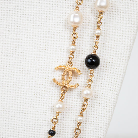 Necklace with pearls, black beads, and gold chain with Chanel logo on a white background