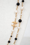 Necklace with pearls, black beads, and gold chain with Chanel logo on a white background