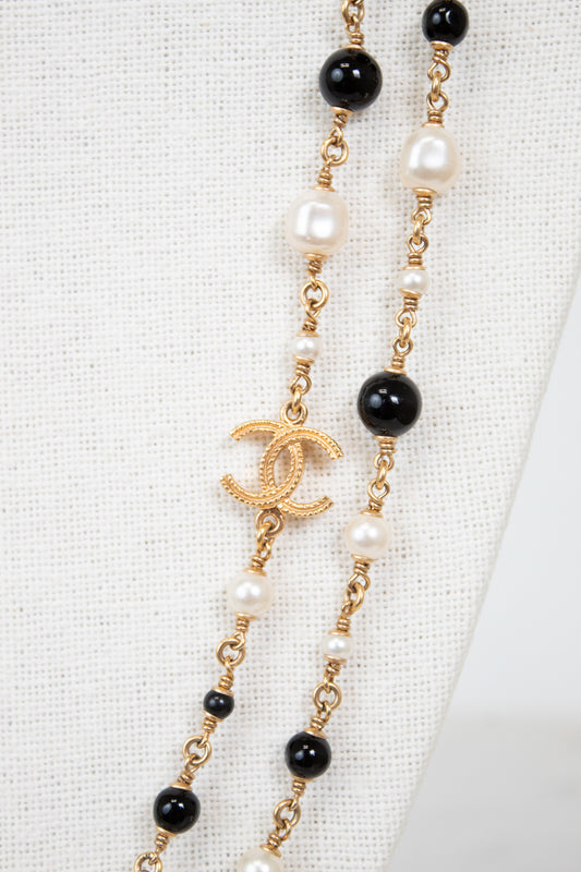 Necklace with pearls, black beads, and gold chain with Chanel logo on a white background