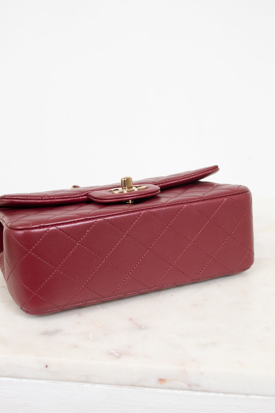 A quilted red leather handbag with gold-tone hardware, resting on a white marble surface against a white background.