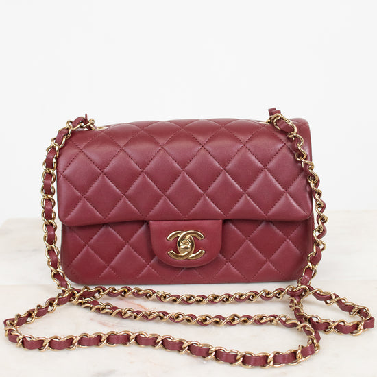 A classic quilted flap shoulder bag in burgundy leather with a gold-tone interlocking CC logo and a gold chain strap, displayed on a light marble surface against a white background.