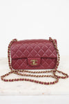 A classic quilted flap shoulder bag in burgundy leather with a gold-tone interlocking CC logo and a gold chain strap, displayed on a light marble surface against a white background.