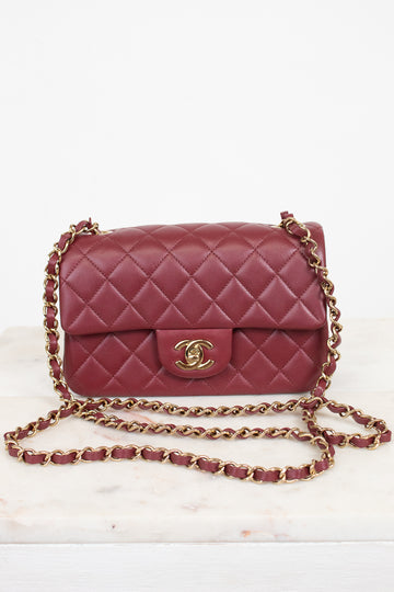 A classic quilted flap shoulder bag in burgundy leather with a gold-tone interlocking CC logo and a gold chain strap, displayed on a light marble surface against a white background.
