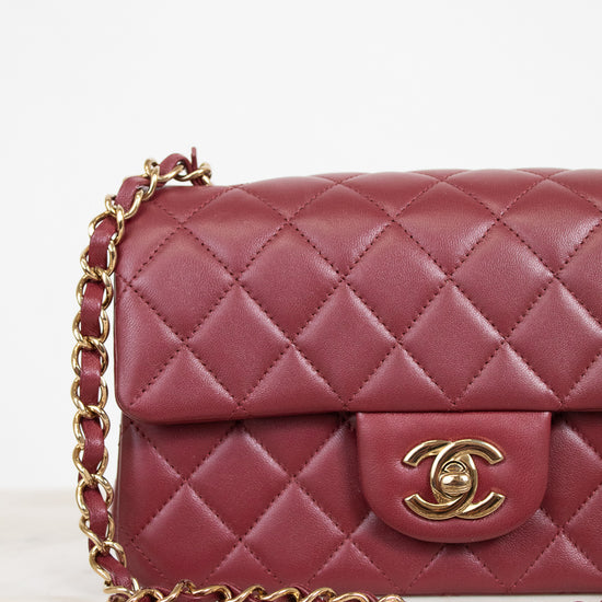 A close-up of a quilted burgundy leather handbag with a gold-tone interlocking CC clasp and a matching burgundy and gold chain strap, set against a clean white background.