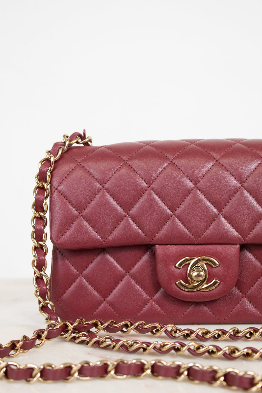 A close-up of a quilted burgundy leather handbag with a gold-tone interlocking CC clasp and a matching burgundy and gold chain strap, set against a clean white background.