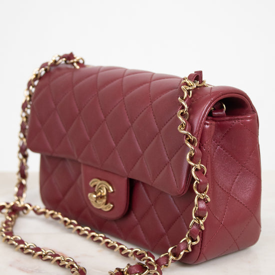 A quilted burgundy leather shoulder bag with a gold-tone chain strap and a gold interlocking CC logo, displayed on a light marble surface against a white background.