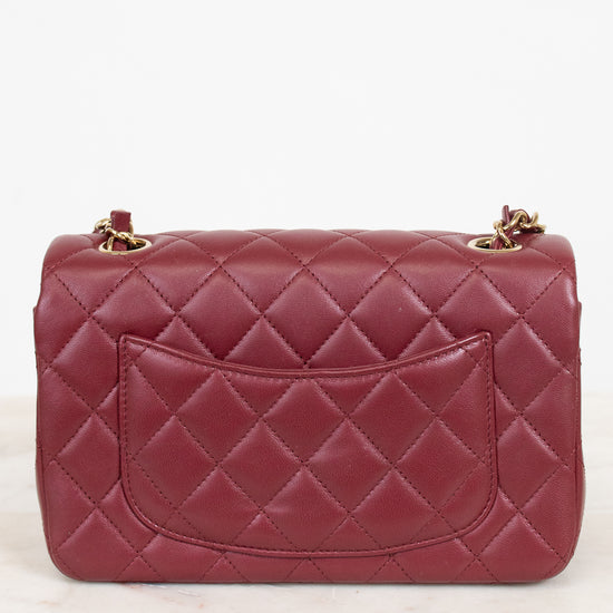 A quilted burgundy leather handbag with gold-tone chain strap hardware, shown from the front on a light marble surface against a white background.