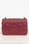 A quilted burgundy leather handbag with gold-tone chain strap hardware, shown from the front on a light marble surface against a white background.
