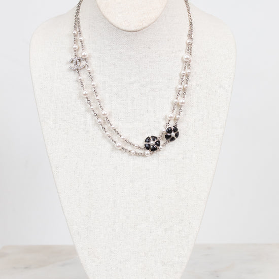 A double-strand silver-toned necklace displayed on a white fabric jewelry bust. The necklace features small silver beads, a silver chain with clear rhinestones, and two black floral cluster charms with clear rhinestones.