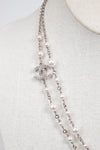A Chanel double-strand pearl necklace with a silver-tone CC logo charm encrusted with clear crystals, displayed on a cream-colored fabric mannequin bust.